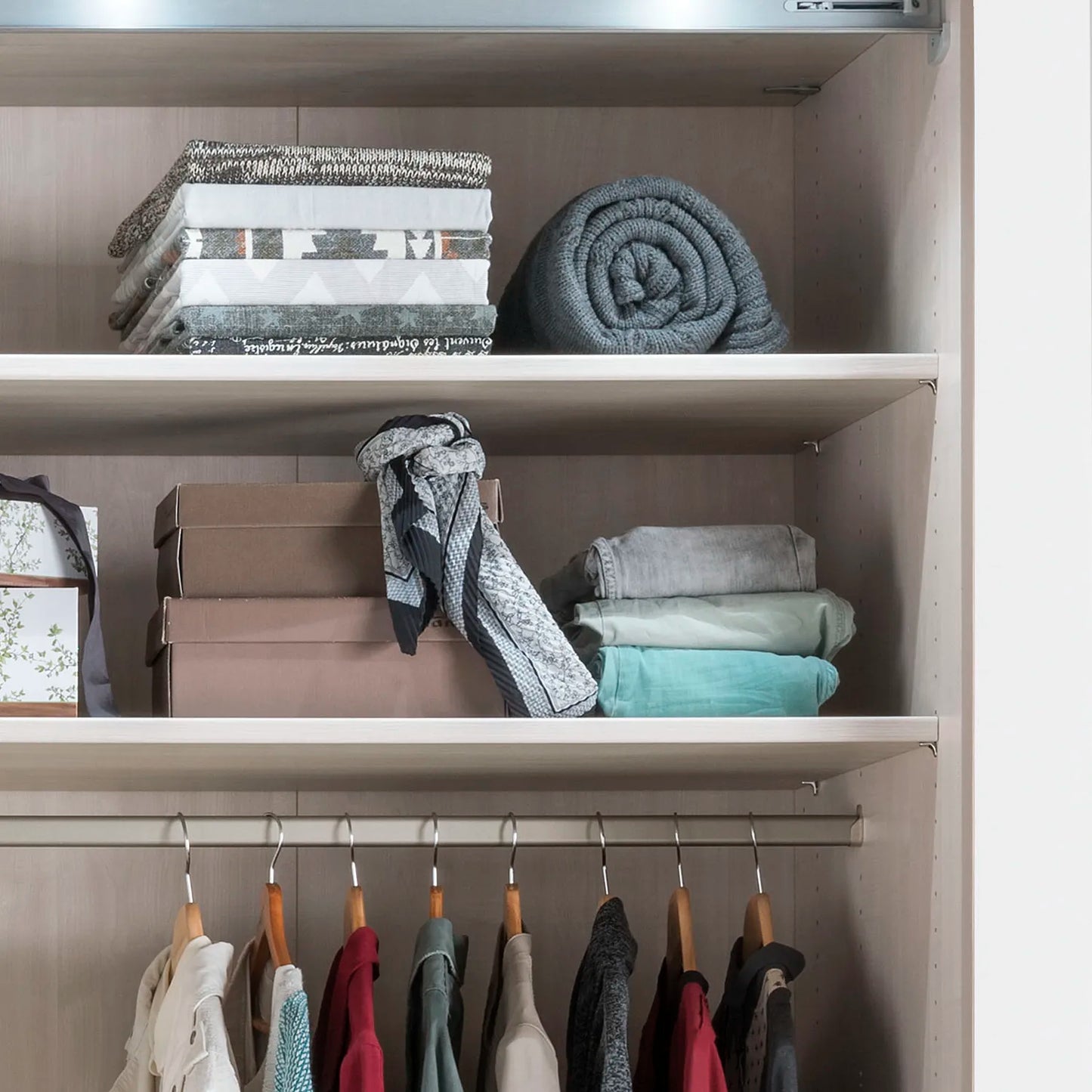 Closet with shelves containing folded clothes and a hanging rack with garments.