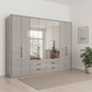 Wiemann Saka 300cm Bi-Fold Wardrobe With 4 Glass Doors & 4 Mirror Doors & 6 Glass Drawers in Glass Pebble Grey styled in a modern bedroom