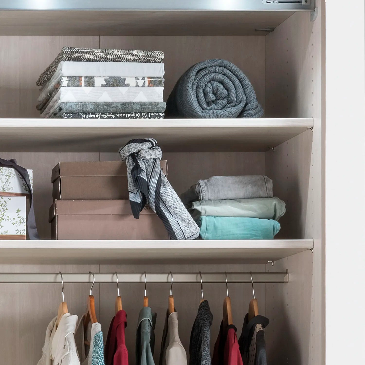 Closet with shelves containing folded clothes and a hanging rack with garments.