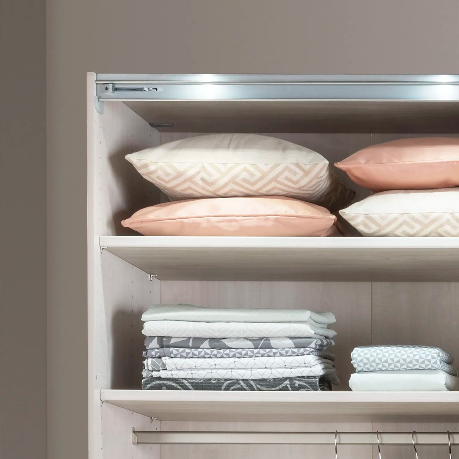 Closet with shelves containing folded clothes and pillows against a neutral wall.