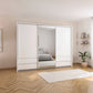 A modern white sliding wardrobe with mirrored doors in a minimalist bedroom setting with light wood herringbone flooring and a white rug.