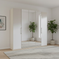 White wardrobe with wooden handles in a room with a plant and framed picture on the wall.