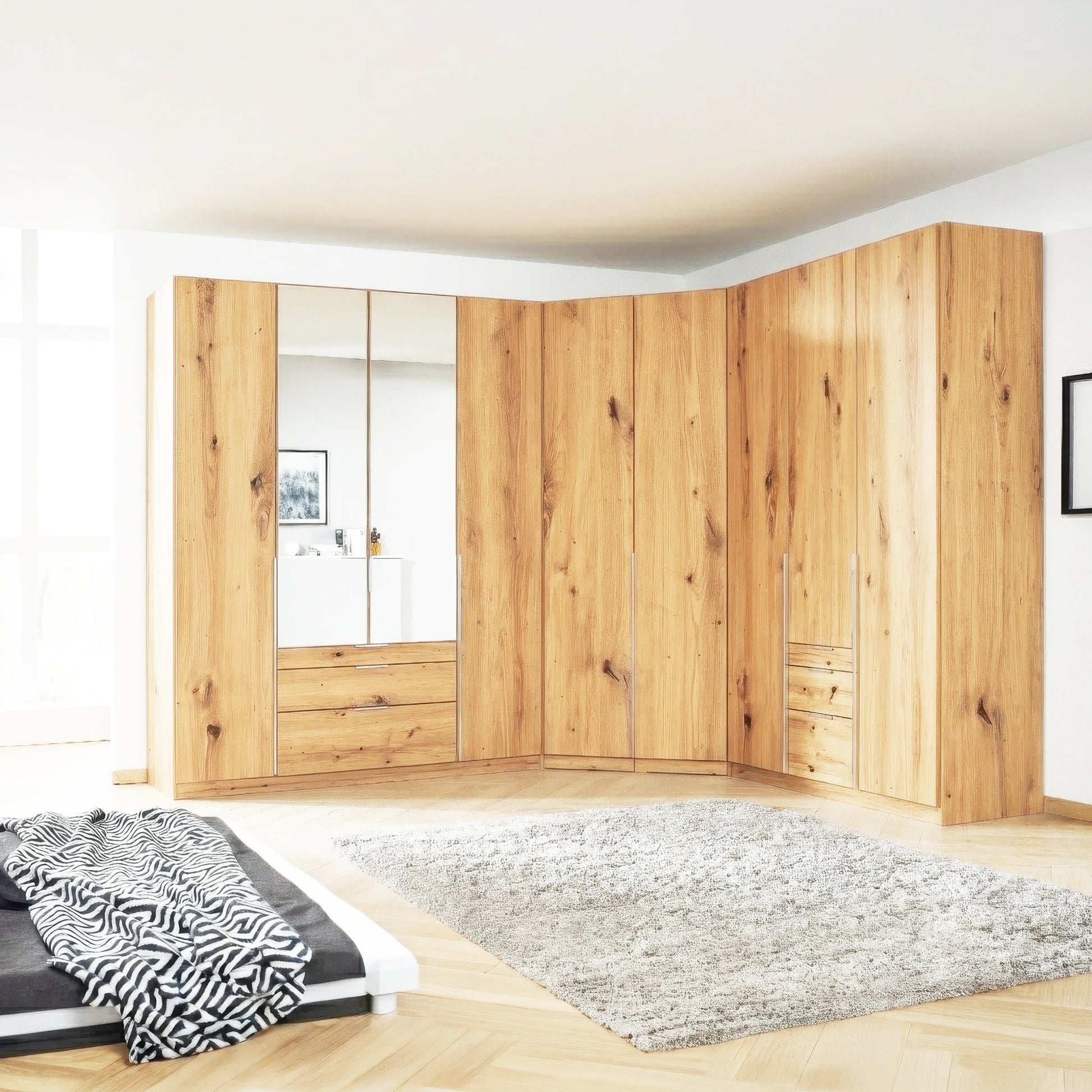 A large modular Corner wardrobe by Rauch made of Artisan wood panels, including mirrored doors and drawers, installed in a bright modern room with a gray rug and bed partially visible.