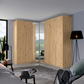 A large corner wardrobe with light natural wood grain doors and mirrored sliding panels, shown in a modern bedroom setting.