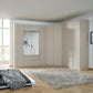 A large modular Rauch Alabama Corner wardrobe system in a light beige wood finish, featuring two mirrored doors, drawers, and tall cabinet doors, installed in a modern bedroom with light wood floors and a gray shag rug.