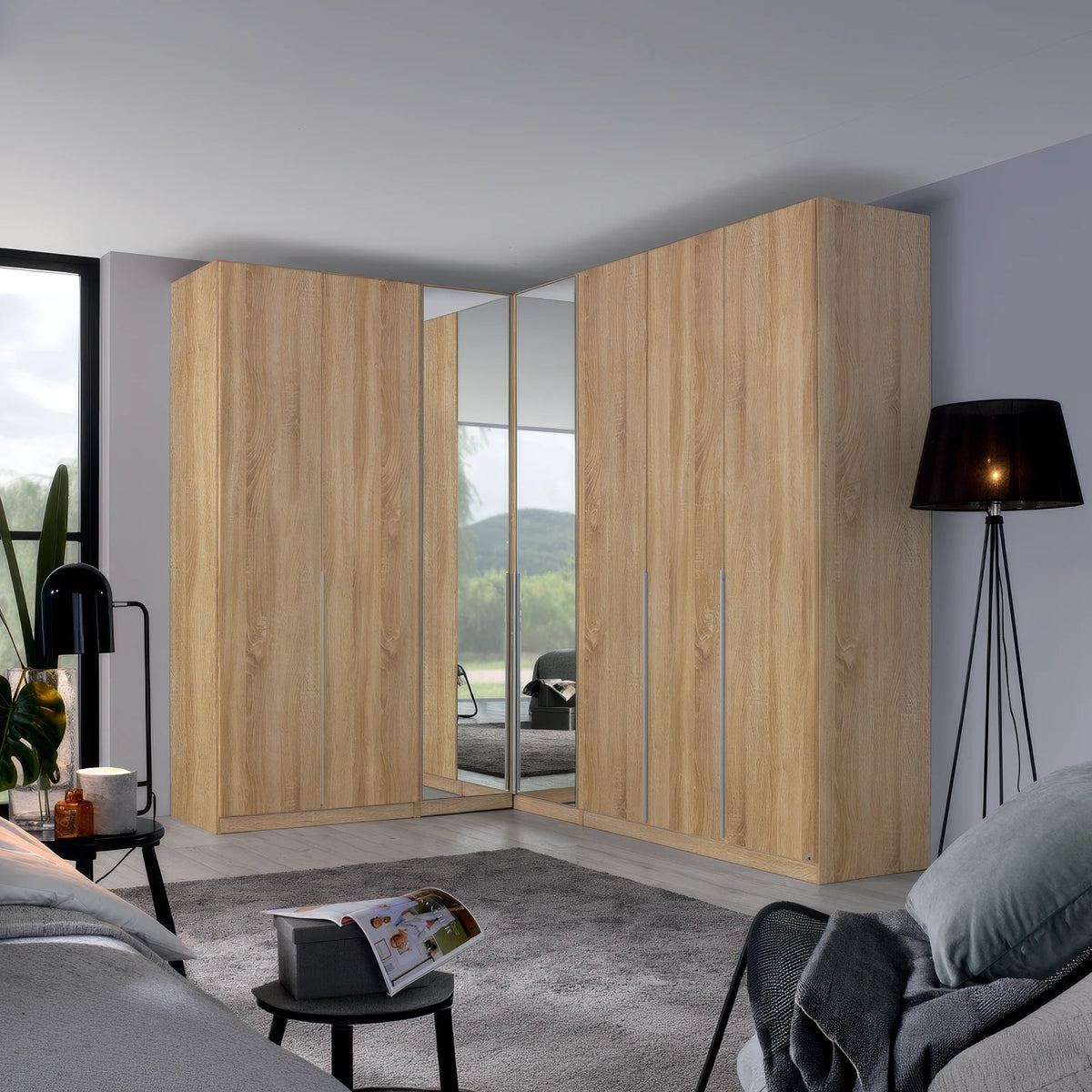 A large corner wardrobe set in a modern bedroom, featuring light oak wood grain doors with mirrored panels on the inner doors to show the bed underneath.