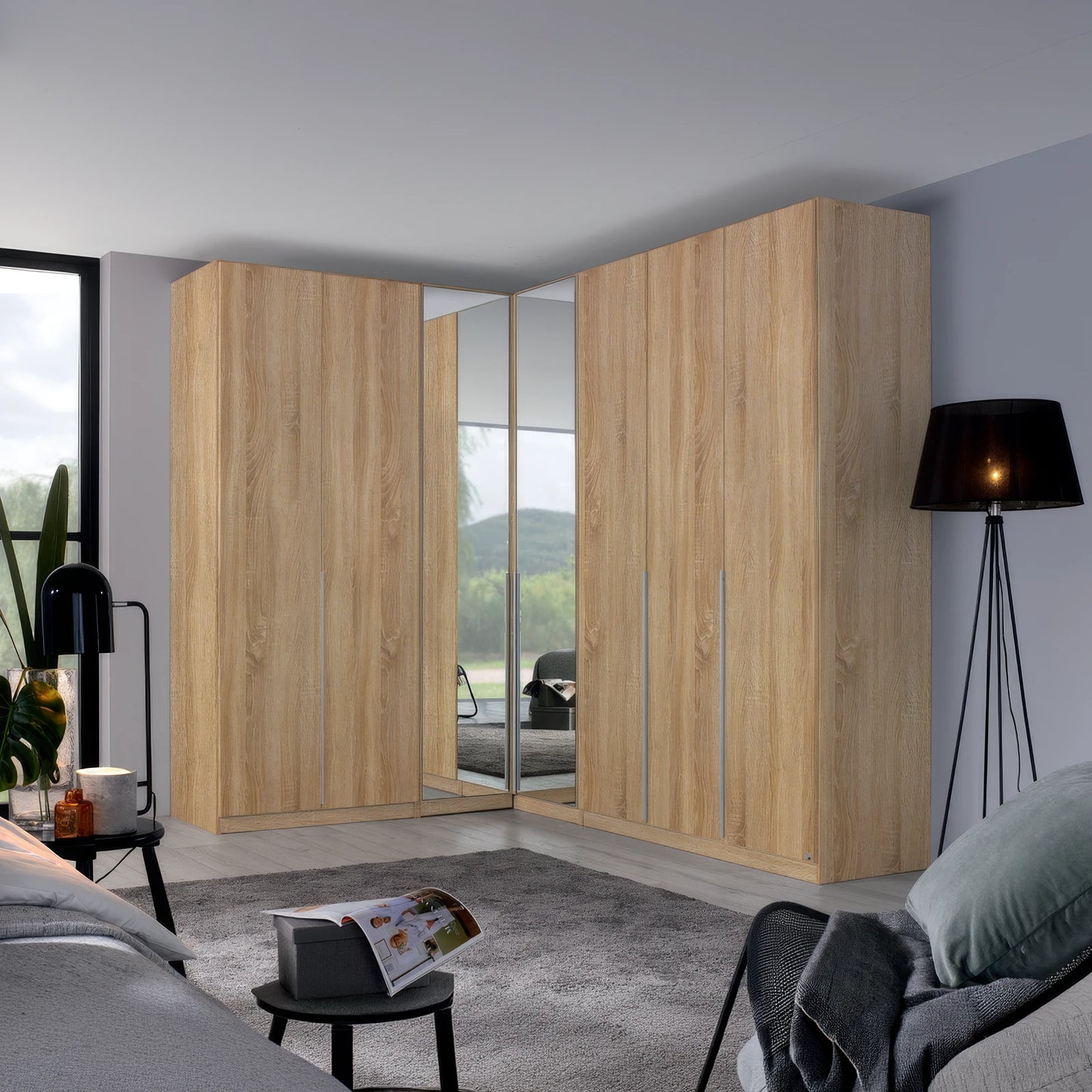 A large corner wardrobe set in a modern bedroom, featuring light oak wood grain doors with mirrored panels on the inner doors to show the bed underneath.