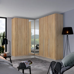 A large corner wardrobe set in a modern bedroom, featuring light oak wood grain doors with mirrored panels on the inner doors to show the bed underneath.
