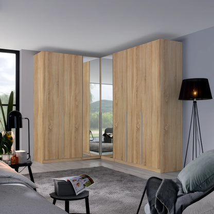 A large corner wardrobe set in a modern bedroom, featuring light oak wood grain doors with mirrored panels on the inner doors to show the bed underneath.