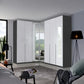 A modern rauch corner wardrobe system with white high-gloss doors and dark gray side panels, installed in a contemporary bedroom setting.
