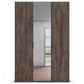 A tall wardrobe or closet door set with a weathered brown wood grain finish, shown partially open to reveal a mirror reflecting a room interior.