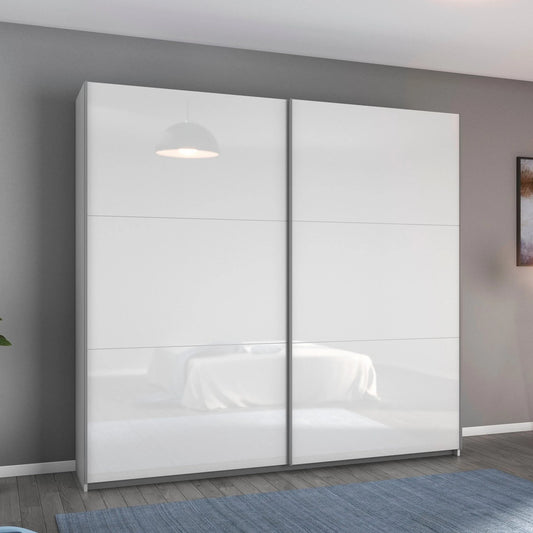 A modern two-door Width 218cm Rauch Aurelia wardrobe with high-gloss white sliding doors, shown in a staged bedroom setting with gray walls, a blue rug, and a wall-mounted abstract painting.