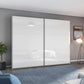 A modern two-door Width 261cm Rauch Aurelia wardrobe with high-gloss white sliding doors, shown in a staged bedroom setting with gray walls, a blue rug, and a wall-mounted abstract painting.