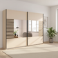 A modern Rauch Barea sliding wardrobe with cream-colored doors and black metal frames, featuring integrated mirrors and decorative slatted side panels, shown in a bright, contemporary room with a potted plant and light-colored rug.