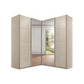 A modern Rauch Quadra Lema corner wardrobe with four doors, including two mirrored doors that reflect an interior room and outdoor scenery. The wardrobe doors have a Champagne finish.