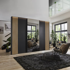 Wiemann Tulsa 3 door graphite sliding wardrobe featuring integrated natural oak wood slatted decking panel and a full-length mirrored central door in a modern bedroom setting.