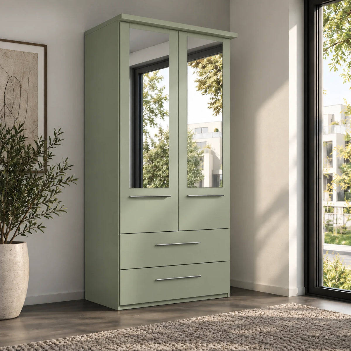 A sage green Wiemann Cairns two-drawer wardrobe with two mirrored upper doors and silver handles, shown in a modern room setting with a window, potted plant, and rug.