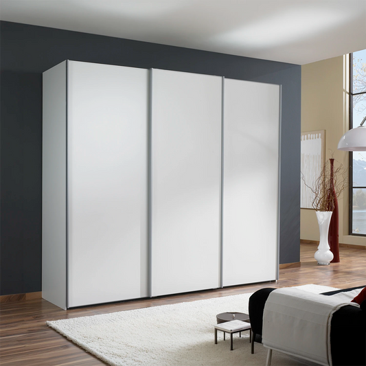 A modern Low height Wiemann Darwin three-door sliding wardrobe with matte white doors, set in a contemporary living room with dark gray and beige walls, wood flooring, and a white rug.