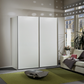 A modern white Wiemann Darwin 197cm High sliding wardrobe with slim metallic frames, set in a styled living room next to a sofa and window.