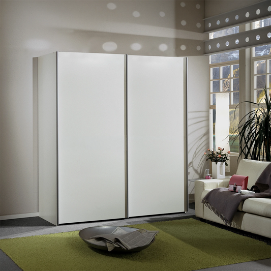 A modern white Wiemann Darwin 197cm High sliding wardrobe with slim metallic frames, set in a styled living room next to a sofa and window.