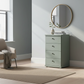 Light green chest of drawers with round mirror in a room with a chair and window.