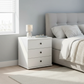 White nightstand with lamp next to a bed in a bedroom