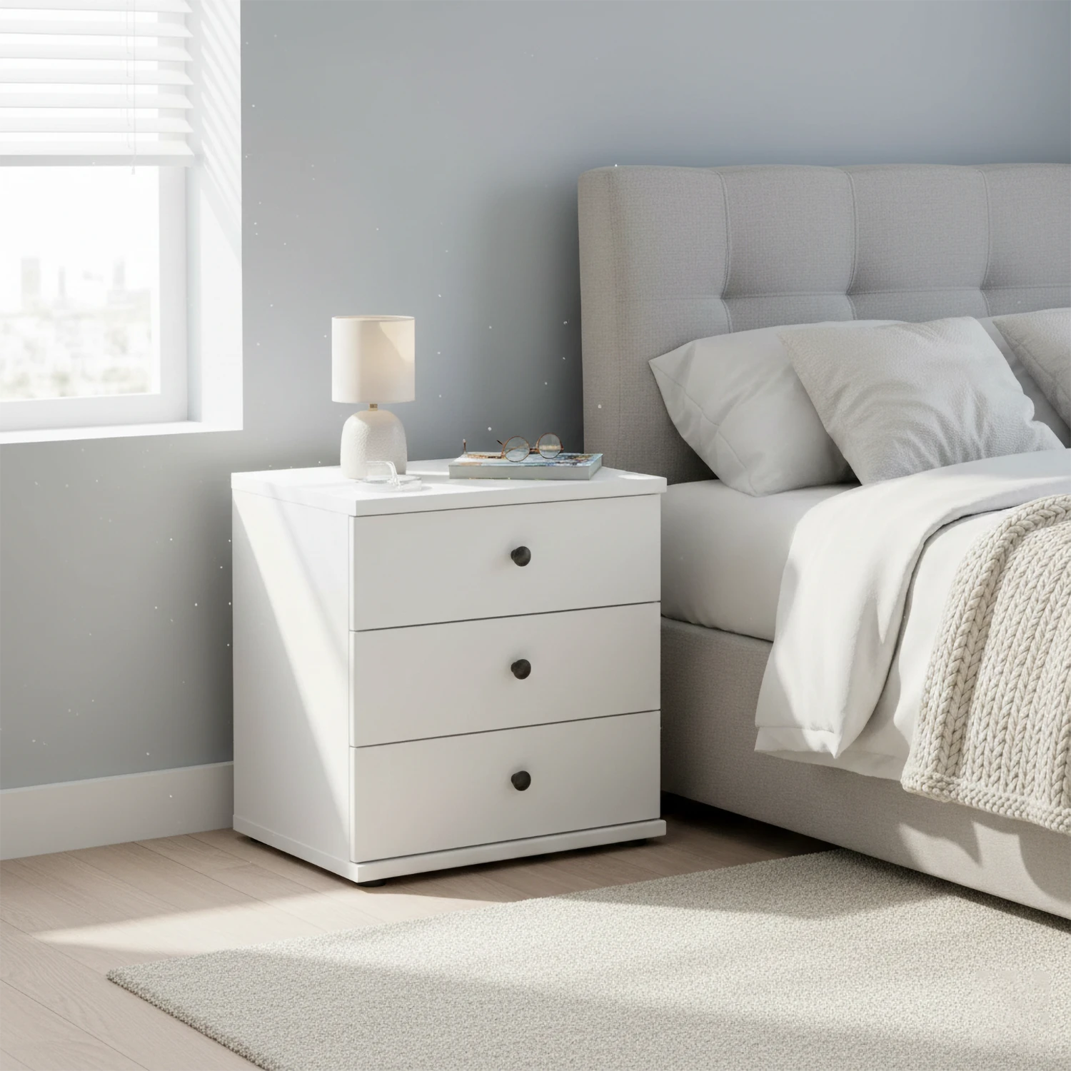 White nightstand with lamp next to a bed in a bedroom