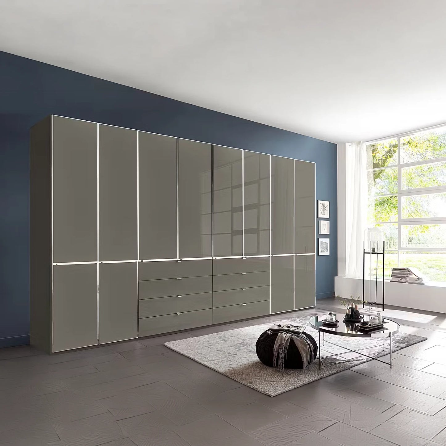A large modern wardrobe or storage cabinet set in a styled living room. The cabinet features a glossy light gray finish with a grid pattern on the upper doors and multiple drawers on the lower section.