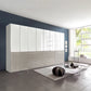 A large modern ceiling High storage cabinet wardrobe in gloss white glass and Pebble glass finish, featuring high doors and lower drawers, installed in a contemporary living room with a dark blue accent wall and gray tiled floor.