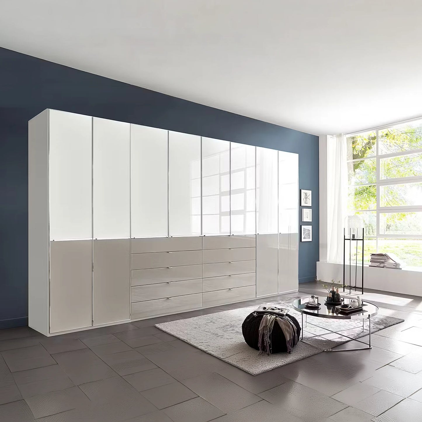 A large modern ceiling High storage cabinet wardrobe in gloss white glass and Pebble glass finish, featuring high doors and lower drawers, installed in a contemporary living room with a dark blue accent wall and gray tiled floor.