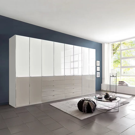 A large modern ceiling High storage cabinet wardrobe in gloss white glass and Pebble glass finish, featuring high doors and lower drawers, installed in a contemporary living room with a dark blue accent wall and gray tiled floor.
