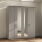 A tall four-door Wiemann Truro wardrobe in a Pebble Grey finish with two mirrored doors, shown in a real bedroom setting with wood flooring and beige walls.