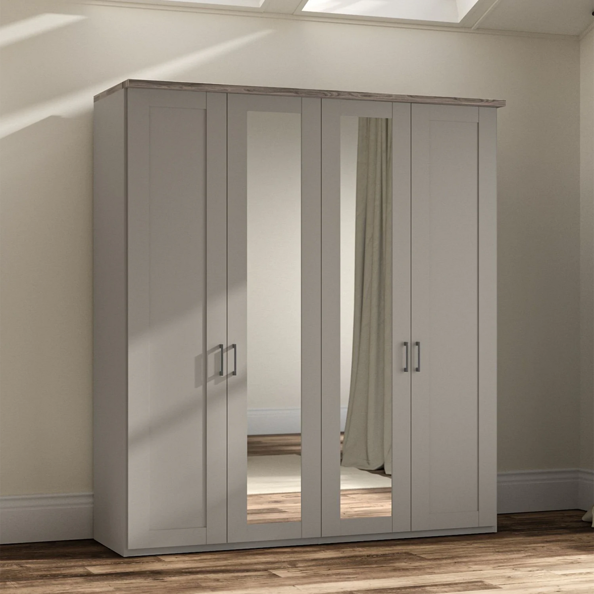 A tall four-door Wiemann Truro wardrobe in a Pebble Grey finish with two mirrored doors, shown in a real bedroom setting with wood flooring and beige walls.