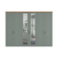 A large six-door wardrobe in a muted sage green colour with a natural light wood top and slate handles. Two of the doors have Mirror panels showing a reflection of a bedroom interior.