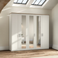 A large white five-door Wiemann Truro wardrobe with three mirrored doors and two solid doors, topped with a light wood grain surface, shown in a bright room with wood flooring and skylights.